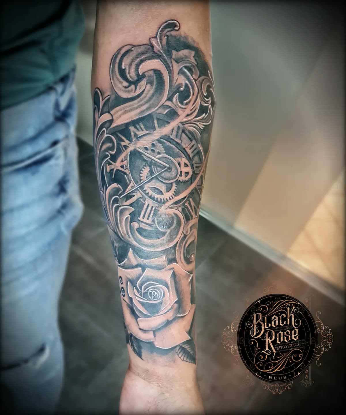 Antebrazo en negro y gris: reloj de bolsillo con engranajes, filigrana barroca y una rosa